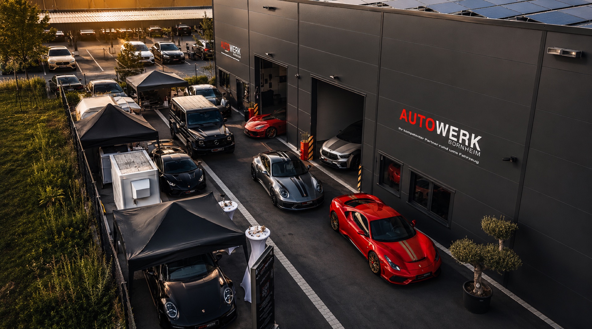 AUTOWERK BORNHEIM Außenansicht bei Sonnenuntergang mit Ferrari und Sportwagen